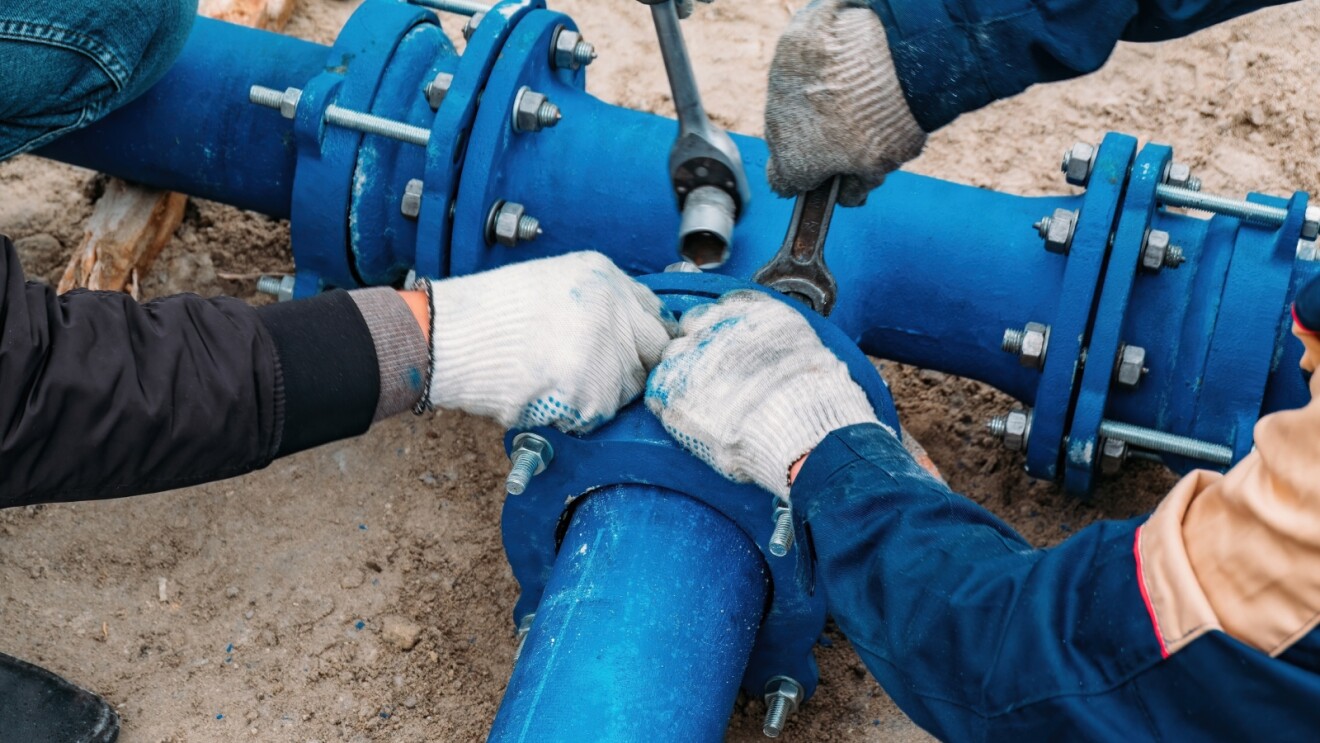 A close-up view of people wearing gloves working on a blue pipe.  