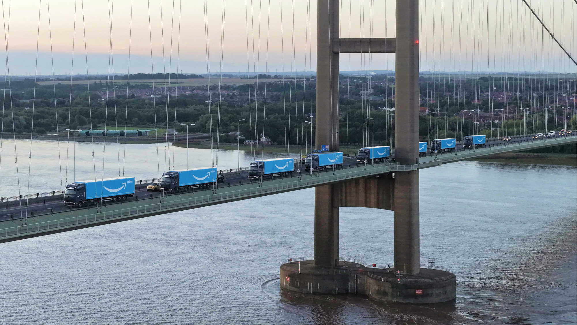 Electric Amazon vehicles drive across a bridge.