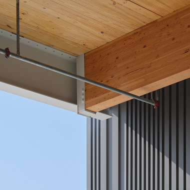 Close-up of wooden ceiling, metal beam, and corrugated steel siding against blue sky.