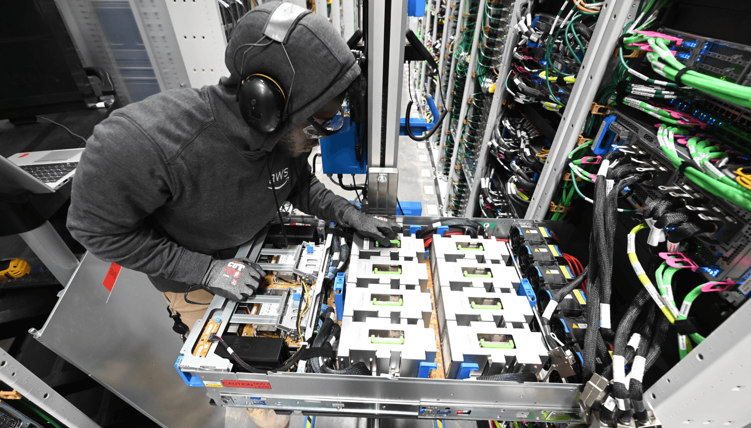 A person wearing headphones and an AWS sweatshirt examines items in a data center.