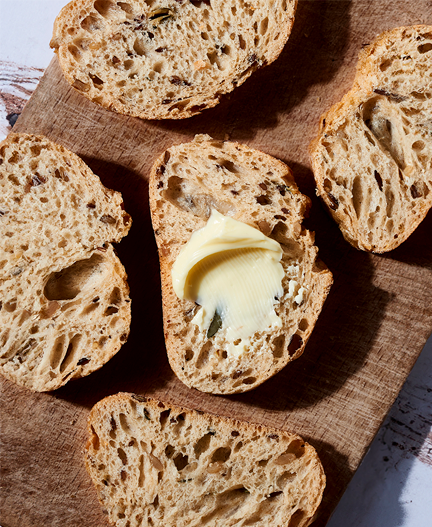 Slices of grainy bread with butter on a wooden cutting board.