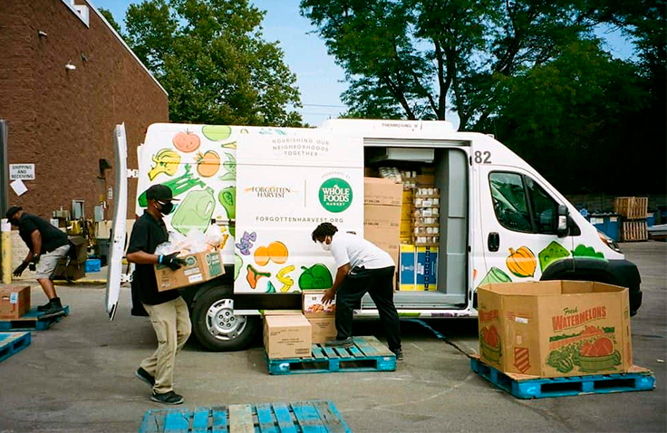 Three people move crates of groceries in front of a Whole Foods Market van.