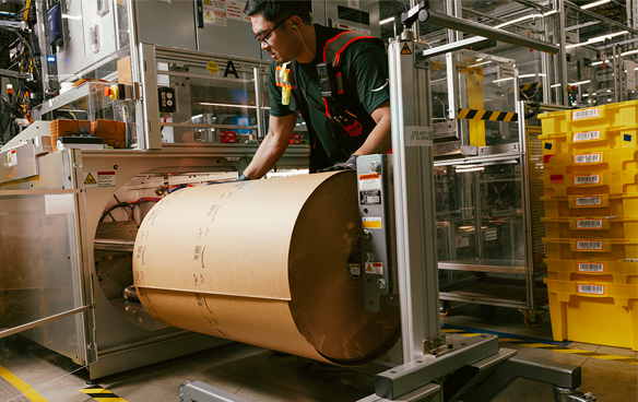 A person wearing an Amazon T-shirt works with a large roll of paper on a machine.