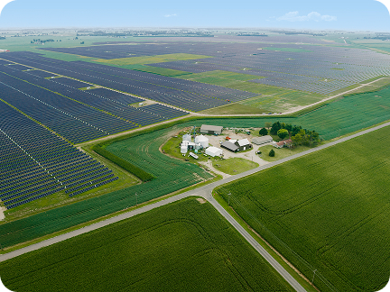 A solar farm surrounds a rural farm amongst lush, green fields. 
