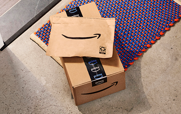 An Amazon box and a paper padded mailer sit on a doorstep.