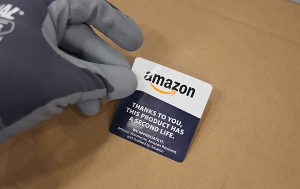 A hand puts a sticker on carboard which states: "Thanks to you, this product has a second life. We appreciate it."