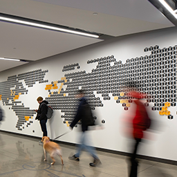 An image of blurred people walking in front of a wall with the map of the world on it.