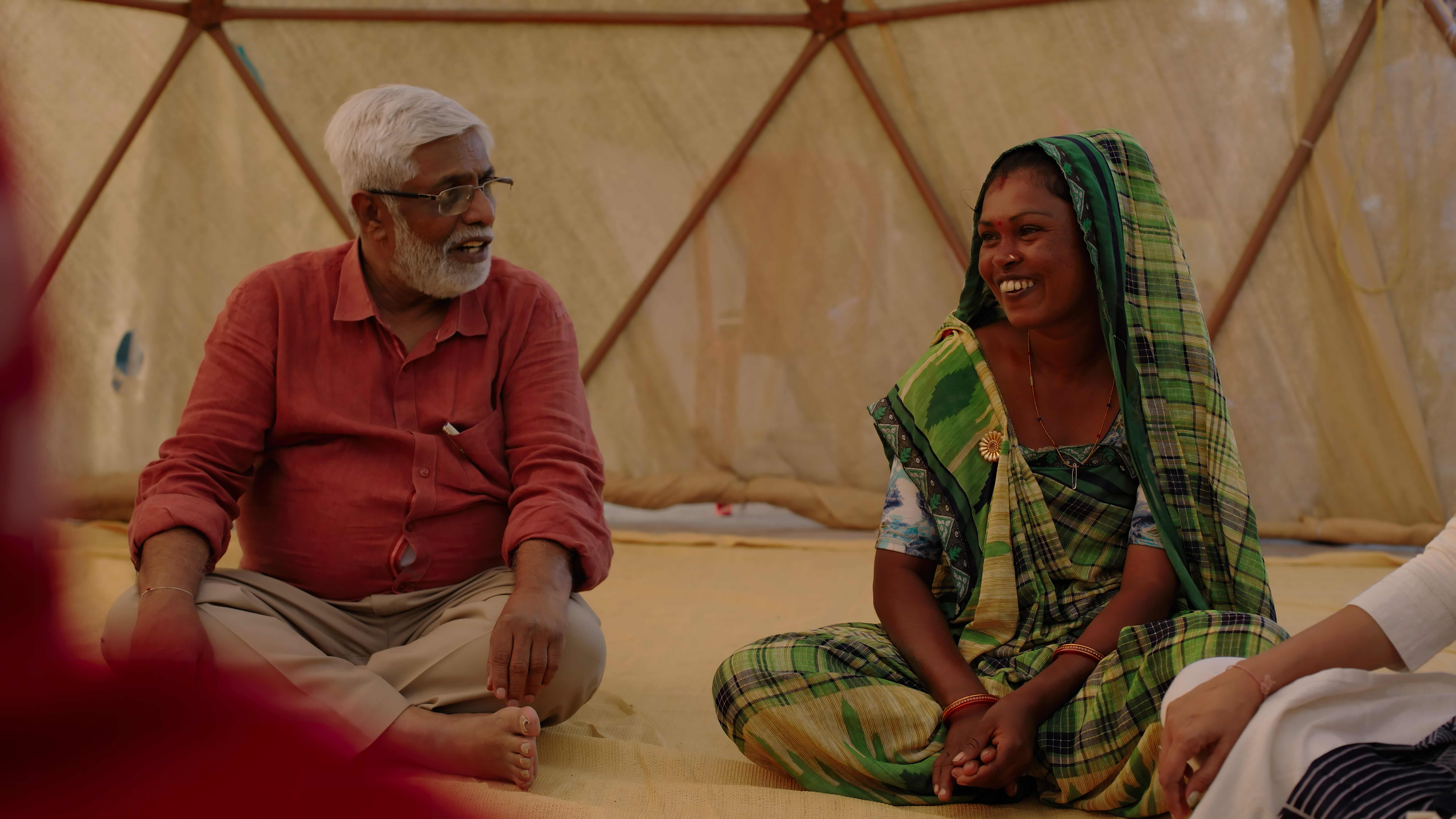 Two people sit on the floor, smiling at each other. 
