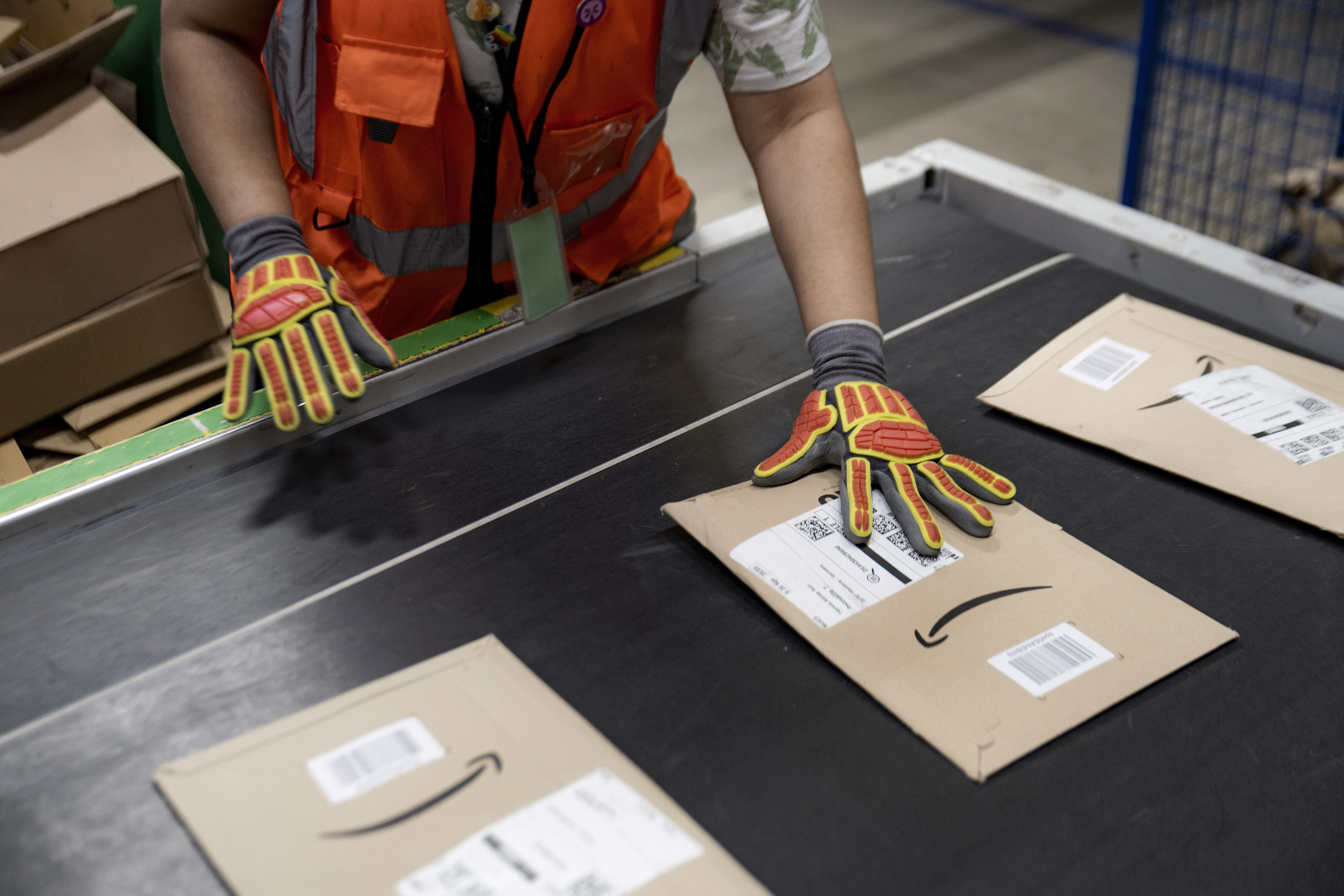 A person wearing gloves places a shipping label on a paper mailer on a conveyor belt. 
