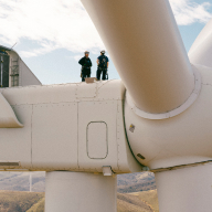  Two people wearing safety equipment stand on a wind turbine.