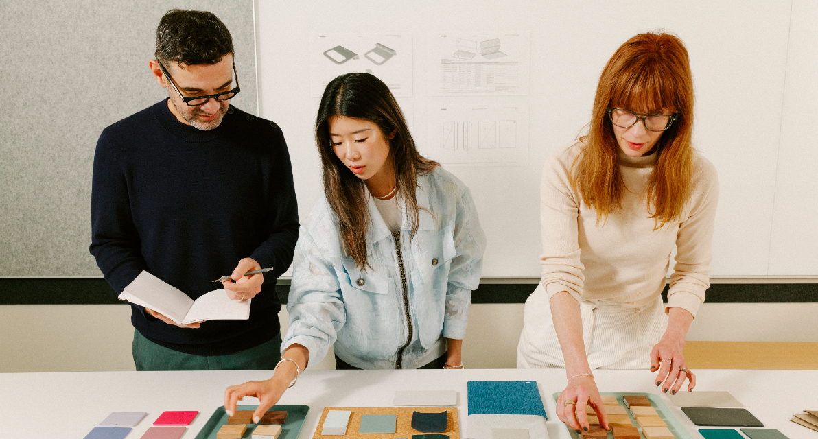 Three people stand over fabric samples.