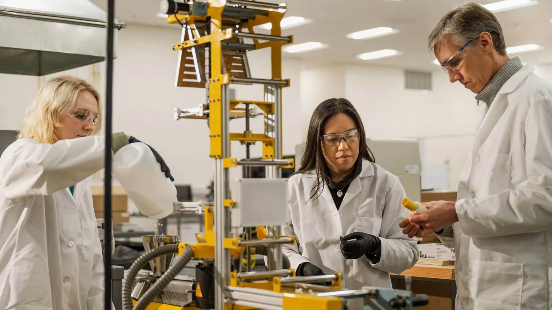 Two people wearing white coats stand in a lab. 