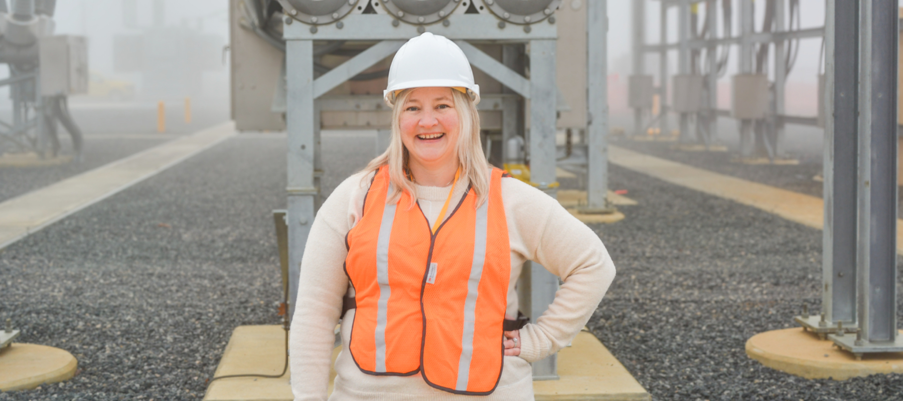 A person stands outside wearing a safety vest, smiling at the camera. 