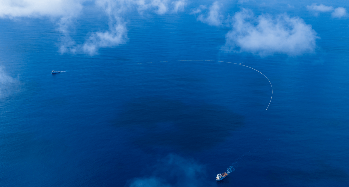 An end-to-end view of a large, submerged net collecting trash in the ocean. 