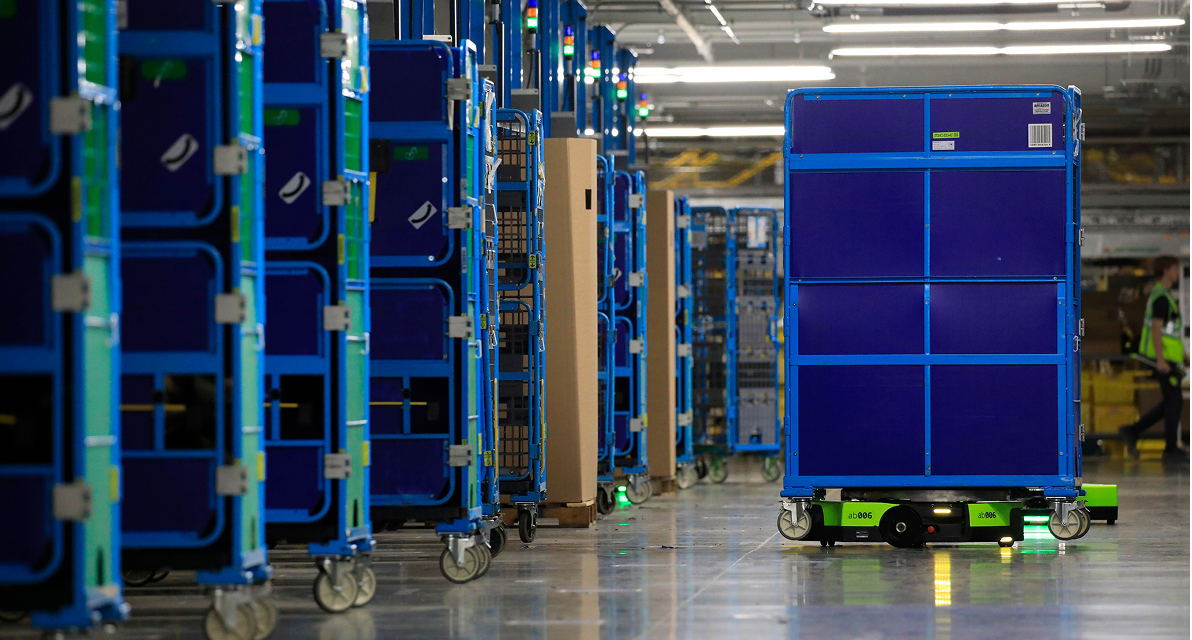A tall blue cart is moved by a robotic device, alongside rows of other carts.