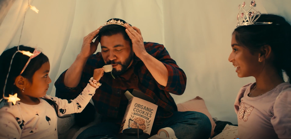 A father and his children play in a tent with a box of organic cookies in between them. 
