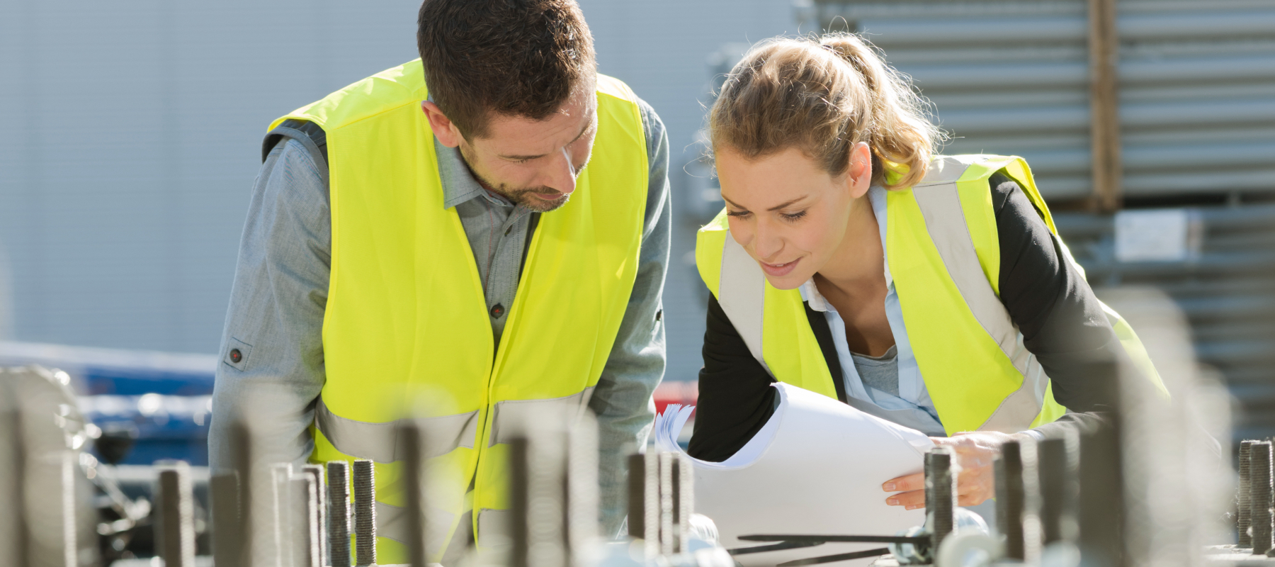 Two people in yellow safety vests look over paperwork together. 
