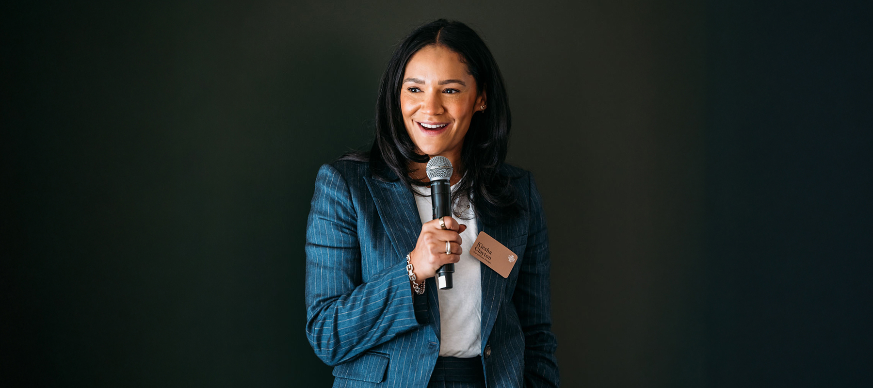 A person stands smiling while holding a microphone. 