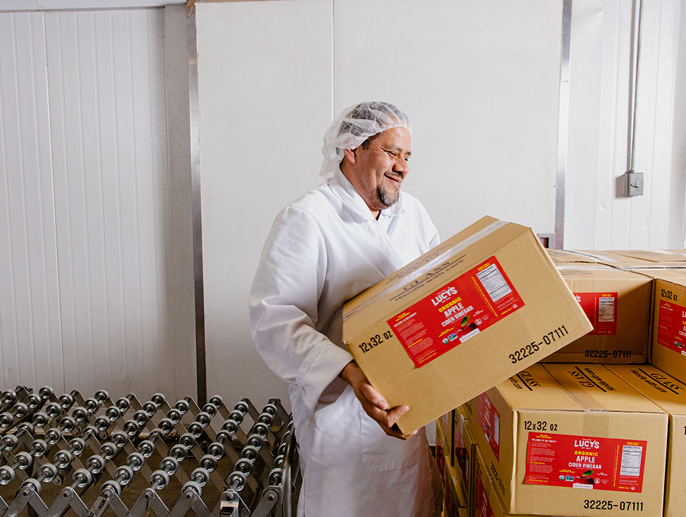 A person wearing protective equipment moves boxes of apple cider vinegar. 